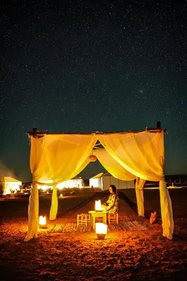 a person sitting under a tent on the beach at night at Merzouga White Camp - Official Luxury Camp in Merzouga