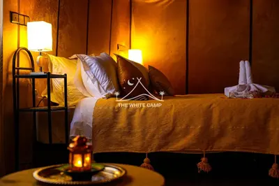 a bedroom with a bed with a white blanket and a table at Merzouga White Camp - Official Luxury Camp in Merzouga