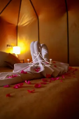 a bed with white towels and pink flowers on the floor at Merzouga White Camp - Official Luxury Camp in Merzouga