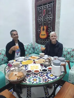 two men sitting at a table with food and a guitar at Riad Fes Colors & SPA - Family Lodging in Fès