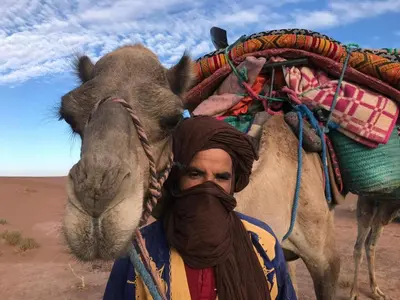 a man is standing next to a camel at AUBERGE KACHTi in Mhamid