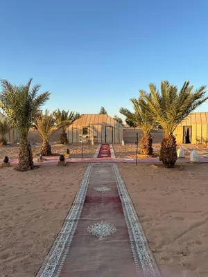a pathway in the middle of a desert with palm trees at Erg Chebbi Sahara Camp in Merzouga