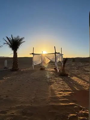 a boat on the beach with the sunset in the background at Erg Chebbi Sahara Camp in Merzouga