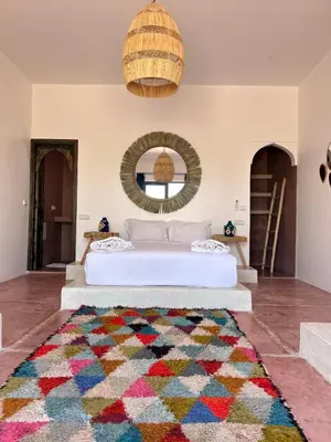 a bedroom with a white bed with a colorful rug at Aghmat Lodge Guest house in Marrakech