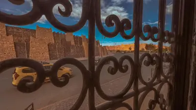 a view of a street through a fence with a yellow taxi at Hotel Rayyan l 'Escale in Ouarzazate