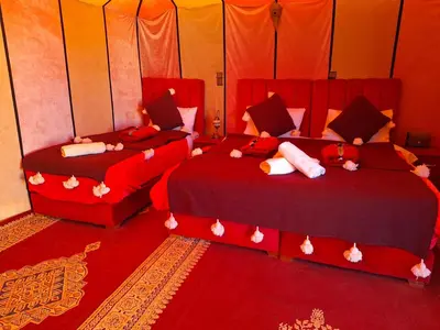two beds in a room with red sheets and pillows at nomad luxury camp in Merzouga