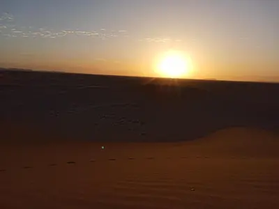 a sunset in the desert with the sun setting at BiVOUAC CÔTE-IRIKI in Foum Zguid