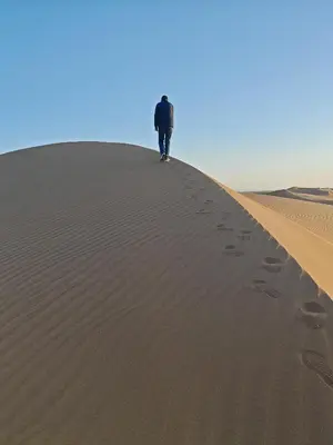 a man walking up a sand dune in the desert at BiVOUAC CÔTE-IRIKI in Foum Zguid