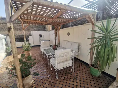 an outdoor patio with white chairs and a pergola at Charmant appartement avec terrasse privee a fes medina in Fès
