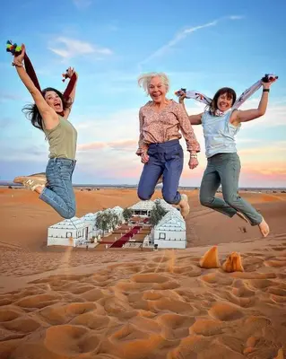 a group of three women jumping in the sand at Ahlam Luxury Camp in Merzouga
