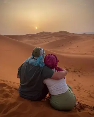 a man and woman sitting in the desert watching the sunset at Ahlam Luxury Camp in Merzouga
