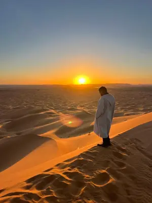 a man standing in the desert watching the sunset at Dream luxury camp in Merzouga