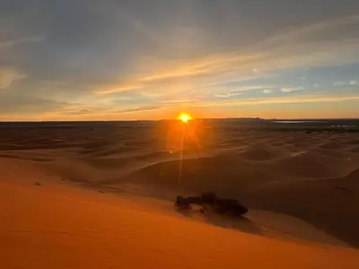 a sunset in the desert with the sun setting at berber desert home for rent in Merzouga