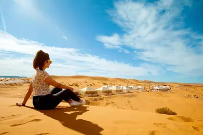 a woman sitting on a sand dune in the desert at berber desert home for rent in Merzouga