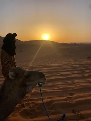 a person with a camel in the desert at sunset at Royal Dune Private Tent in Merzouga