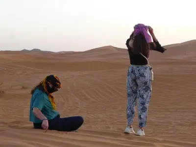 two women sitting in the sand in the desert at Royal Dune Private Tent in Merzouga