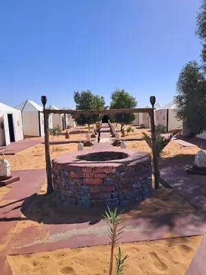 a stone fountain in a courtyard with trees and buildings at Royal Dune Private Tent in Merzouga