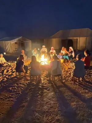 a group of people sitting around a fire in front of a tent at Authentic Desert Camp in Merzouga