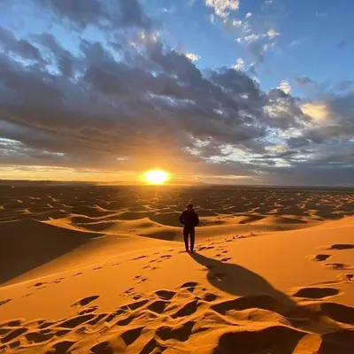 a man walking in the desert at sunset at Authentic Desert Camp in Merzouga