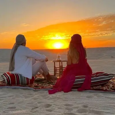 a man and woman sitting on the beach watching the sunset at Authentic Desert Camp in Merzouga