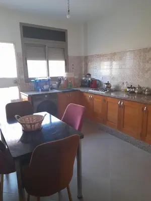 a kitchen with wooden cabinets and a table with chairs at Appartement meublé ennasr49 in Khenifra