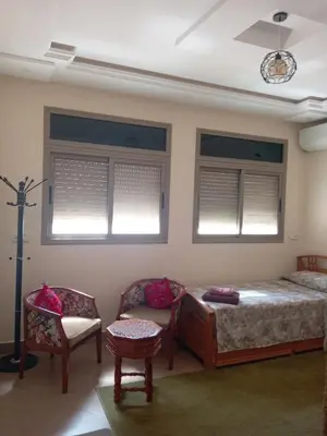 a bedroom with a bed and a chair and windows at Appartement meublé ennasr49 in Khenifra