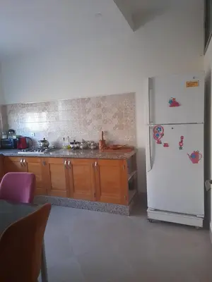 a kitchen with a white refrigerator and wooden cabinets at Appartement meublé ennasr49 in Khenifra