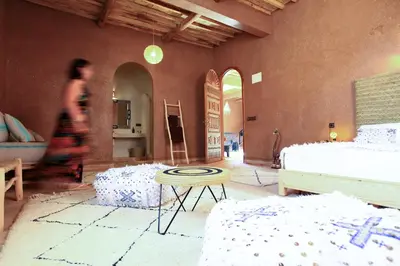 a woman walking through a room with two beds and a table at Riad Dar Tiziri in Zagora