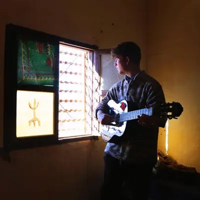 a young man playing a guitar in front of a window at Dar Nomad Tagounite in Zagora