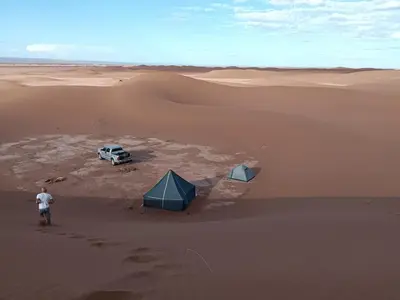 a man standing in the desert with a tent and a truck at Bivouac beauté du désert in Mhamid