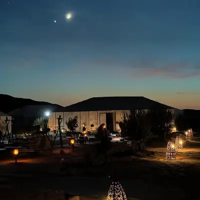 a man standing in front of a tent at night at Erg Chebbi Desert Luxury Camp in Merzouga