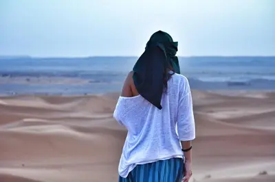 a woman walking through the desert at Erg Chebbi Desert Luxury Camp in Merzouga