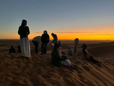 a group of people standing on the sand in the desert at Chegaga Desert Trips in Mhamid
