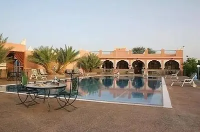 a pool with a table and chairs next to a building at HOTEL BOUGAFER - TAZARINE in Tazzarine