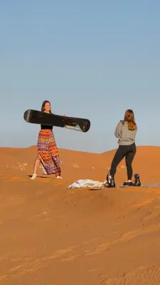 two women walking through the desert with a weapon at Riad Akabar Merzouga in Merzouga