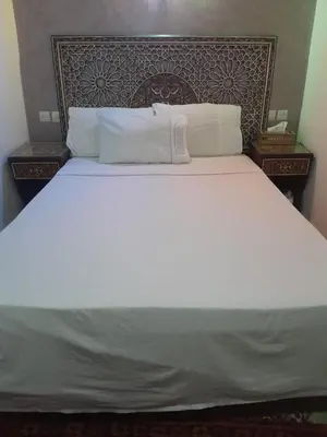 a large bed with white sheets and pillows at famille fahym in Fès