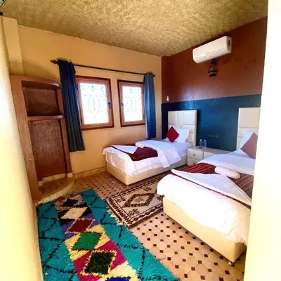 a bedroom with two beds and a rug at Riad Hassi Labied Merzouga in Merzouga
