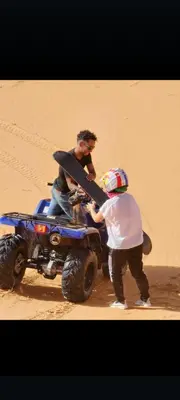 a man and a child standing next to a wheeler in the desert at Khadija Desert Camp in Merzouga