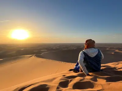 a woman sitting on a sand dune watching the sunset at Desert Erg Chigaga Lodge in El Gouera