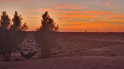 a person in a hammock in the desert at sunset at Sahara Authentic Berber Camp in Mhamid