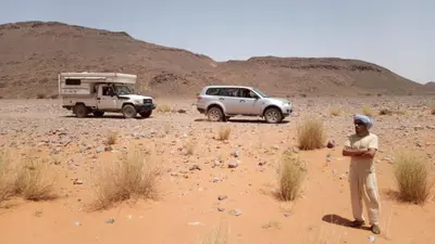 a man standing in the desert with a truck at Auberge Hassi Fougani in Tafraoute Sidi Ali