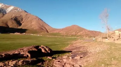 a view of a mountain with a field and a road at Gite Oukaimeden in Oukkainrdem