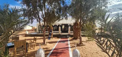 a person standing in front of a building with trees at sahara oasis camp in Merzouga