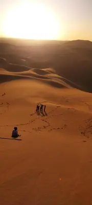 a man sitting in the desert watching the sunset at Erg Chigaga Regency Camp in El Gouera