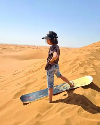 a young boy standing on a surfboard in the desert at Erg Chigaga Regency Camp in El Gouera