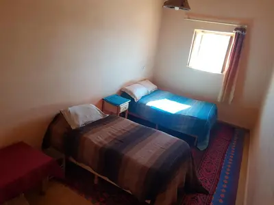 two beds in a small room with a window at Chez Meriem in Merzouga