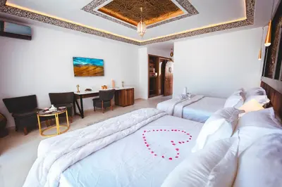 a bedroom with two beds and a dining room with a table at Kasbah Merzouga in Merzouga