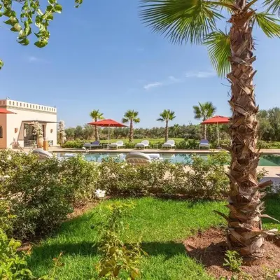 a palm tree next to a swimming pool with umbrellas at Somptueuse Villa louée avec le personnel de maison in Marrakech