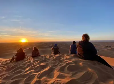 a group of people sitting on top of a sand dune at Erg Chegaga Camp Excursions in Mhamid