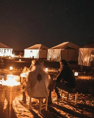 a group of people sitting around a fire at night at Erg Chegaga Camp Excursions in Mhamid